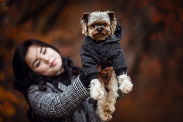 Linda garota jovem com cachorro yorkshire terrier no parque no outono. conceito de cuidado e amizade