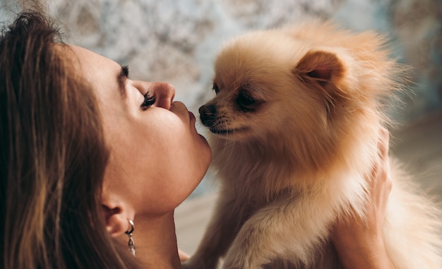 Linda garota jovem morena beija seu cachorro spitz da Pomerânia.