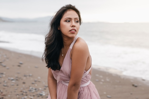 linda garota latina com o bastão preto longo posando em um belo pôr do sol na praia vestida com um vestido de balé rosa