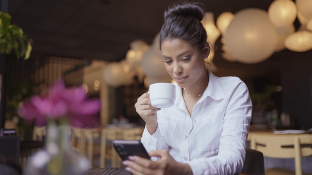 Linda garota latina usando seu celular no café