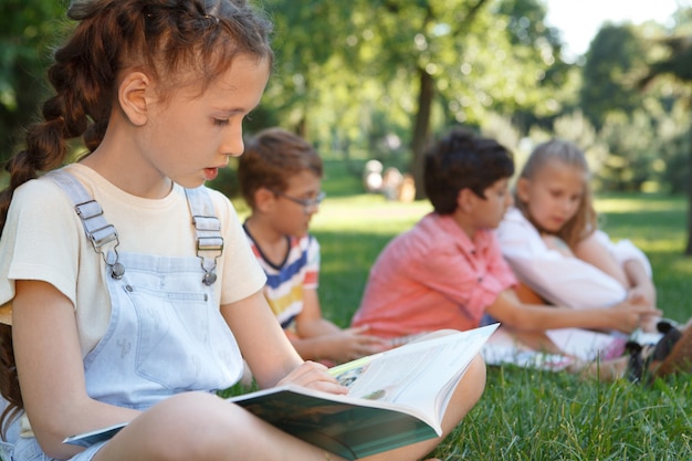 Linda garota lendo um livro ao ar livre no parque em um dia quente de verão