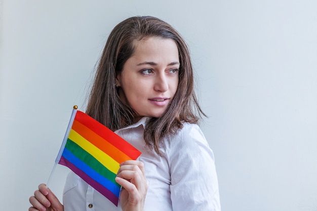 Linda garota lésbica caucasiana com bandeira lgbt do arco-íris isolada no fundo branco, parecendo feliz e animada.