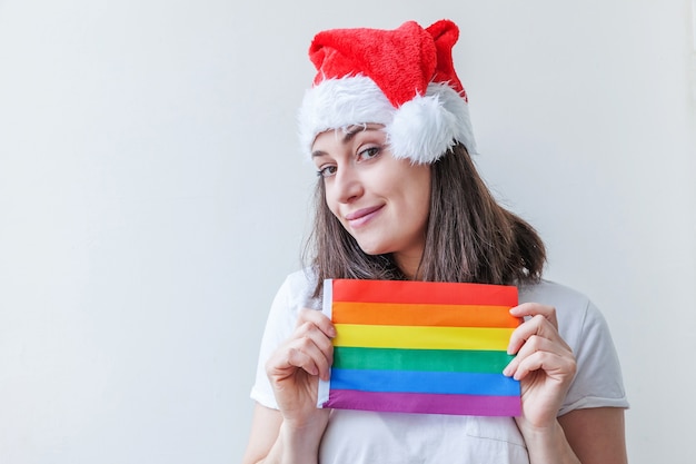 Linda garota lésbica com chapéu de papai noel vermelho com bandeira lgbt do arco-íris isolada