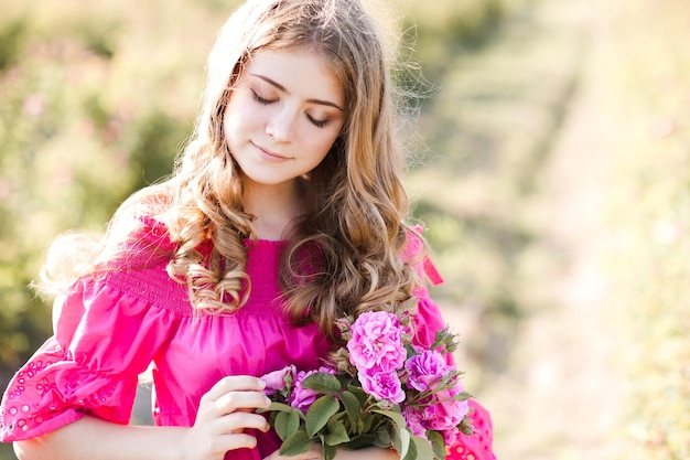 Linda garota loira adolescente usando um vestido rosa segurando uma flor rosa ao ar livre