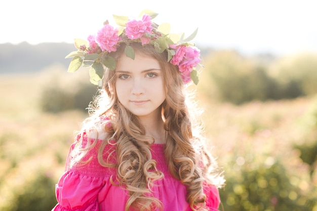 Linda garota loira adolescente usando um vestido rosa segurando uma flor rosa ao ar livre