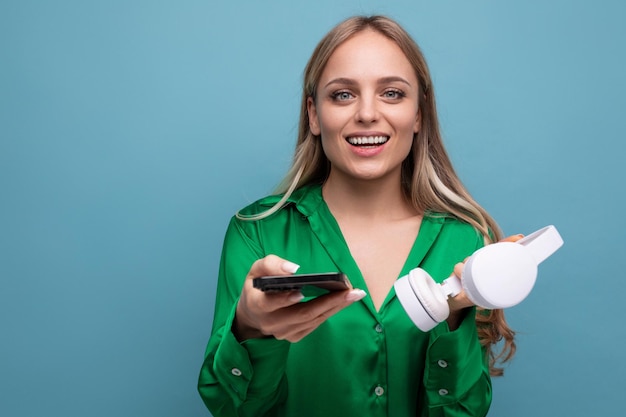 Linda garota loira atraente elegante com fones de ouvido e smartphone em um fundo azul