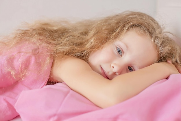 linda garota loira com cabelo encaracolado está deitada em uma cama com roupa de cama rosa