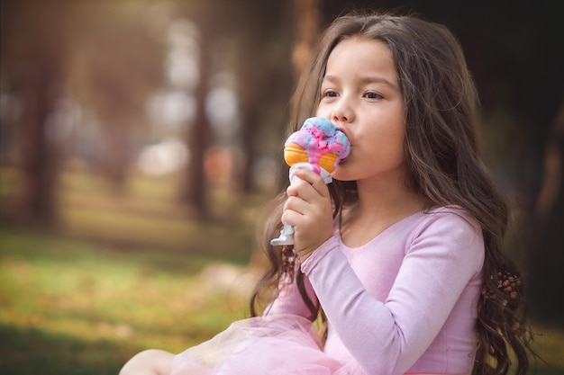 Linda garota loira de cabelos encaracolados comendo um bom sorvete no conceito de parque do dia das crianças