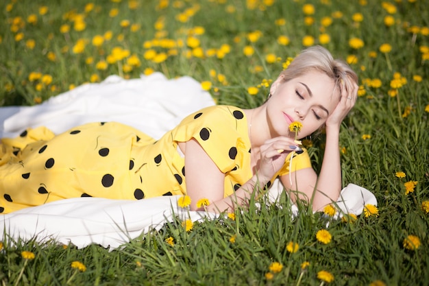 Linda garota loira de vestido amarelo, deitado no jardim florescendo