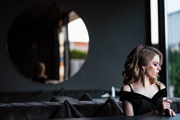 Linda garota loira Retrato de uma jovem em um restaurante Jovem em um restaurante em um fundo preto Retrato de uma garota em um vestido preto Jovem