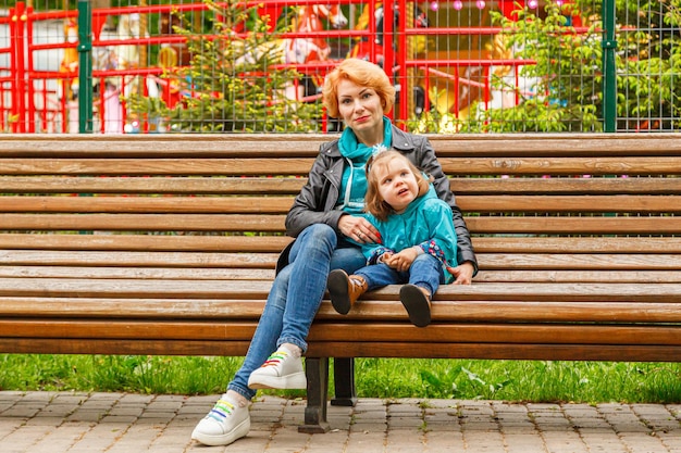 Linda garota mãe com sua filha e filho no parque estão sentados em um banco