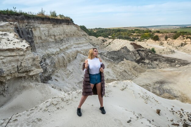 Linda garota morena com camiseta e shorts ocre, casaco de pele, posando em pedras de areia vazias