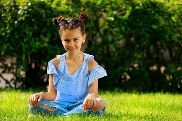 Linda garota morena com uma blusa azul, sentada na grama no verão. Foto de alta qualidade