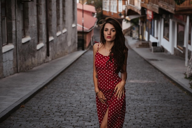 Linda garota morena sexy em um vestido vermelho posando na rua com pedras de pavimentação na Itália