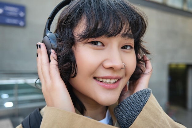 Linda garota morena sorridente ouve música em fones de ouvido e parece feliz com a câmera na rua