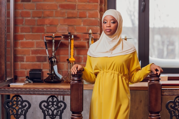 Linda garota muçulmana em hijab sorrindo, esperando por sua comida em um restaurante.