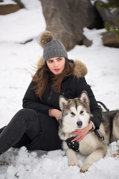 Foto linda garota na floresta de inverno com o cachorro. brinque com o cão husky siberiano.