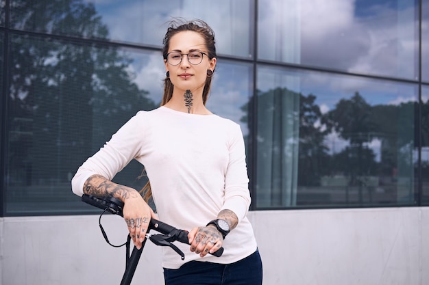 Linda garota na moda com dreadlocks está dirigindo eletro scooter na rua em dia nublado de verão.