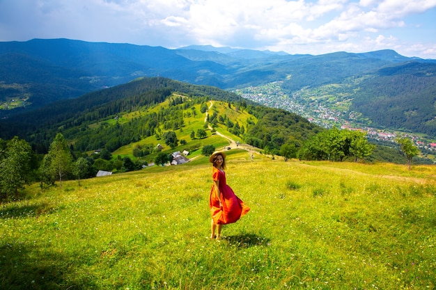 Linda garota nas montanhas. Mulher de vestido de linho e chapéu de palha viajando. Natureza incrível de verão ao redor. Conceito de harmonia e desejo de viajar. Estilo rústico natural. Vento soprando para foto dinâmica.