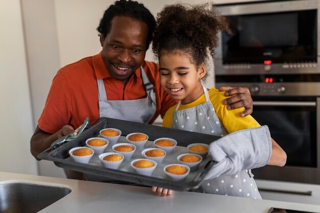 Foto linda garota negra e seu pai segurando a bandeja com muffins na cozinha