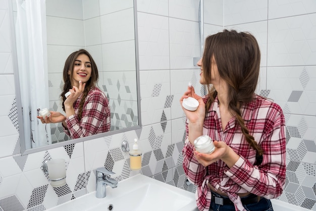 Linda garota no banheiro aplica creme no rosto. conceito de beleza.