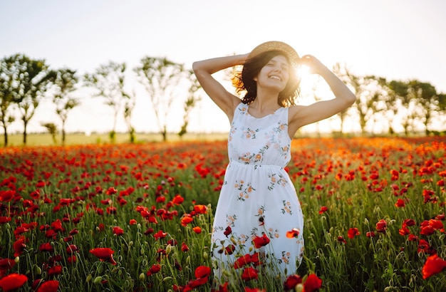 Linda garota no campo de papoulas ao pôr do sol em um vestido branco e chapéu