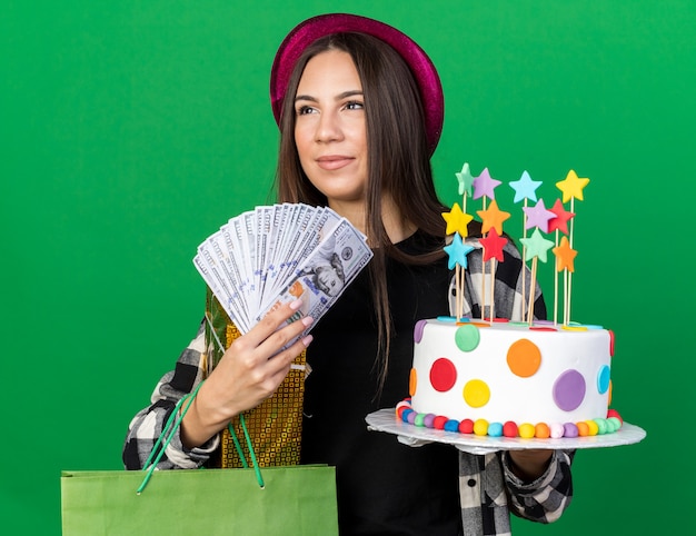Linda garota olhando para o lado com um chapéu de festa segurando um bolo com uma sacola de presente e dinheiro