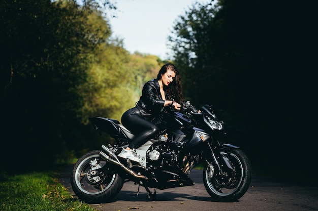 Linda garota perto da motocicleta preta, retrato, na floresta perto da estrada, outono
