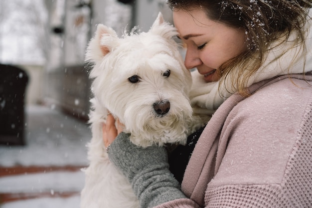 Linda garota rindo abraçando adorável cachorro branco com emoções engraçadas e fofas. terrier branco de montanhas ocidentais. conceito de adoção.