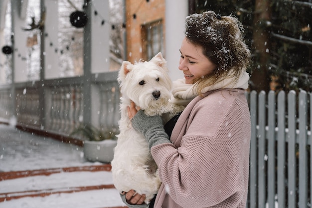 Linda garota rindo abraçando adorável cachorro branco com emoções engraçadas e fofas. Terrier branco de montanhas ocidentais. Conceito de adoção.