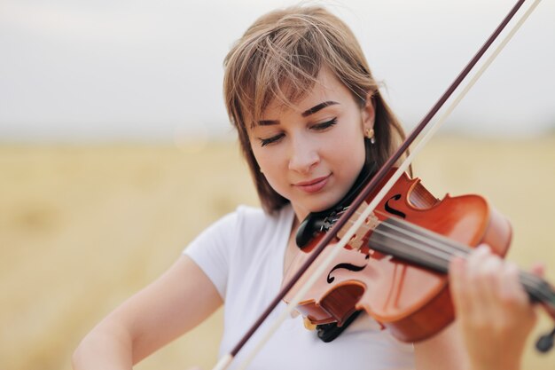 Linda garota romântica com o cabelo solto tocando violino no campo após a colheita