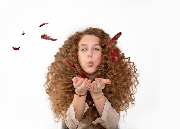 Foto linda garota ruiva cacheada de cabelos longos e ruivos soprando penas com as mãos