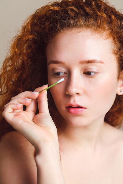 linda garota ruiva remove maquiagem sob os olhos com um cotonete Conceito de cuidados com a pele do rosto