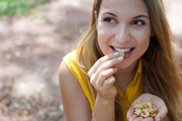 Linda garota saudável comendo castanha de caju no parque olha para o lado