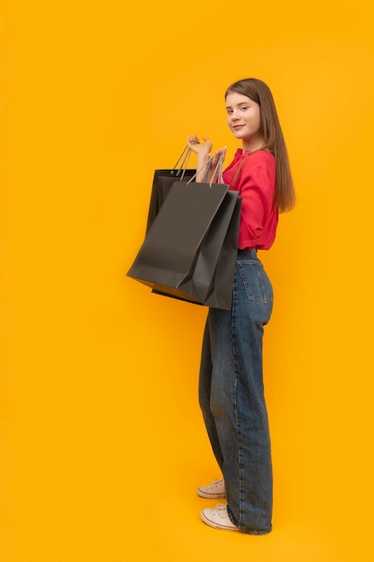 Linda garota segura sacos de papel preto depois de fazer compras em fundo amarelo Black Friday Concept Quadro Vertical