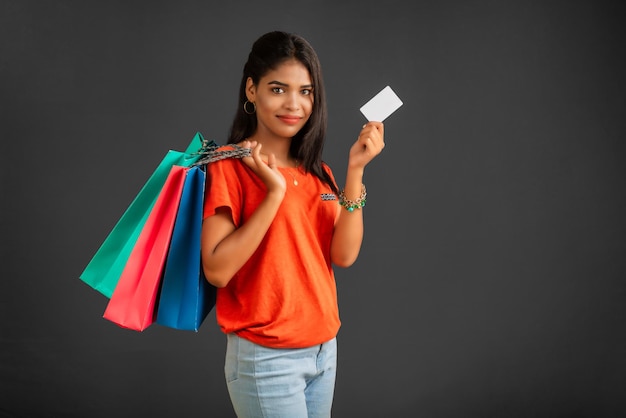 Linda garota segurando e posando com sacolas de compras e cartão de crédito ou débito em um fundo cinza