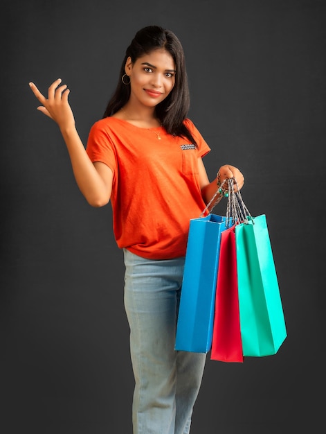 Linda garota segurando e posando com sacolas de compras em um fundo cinza