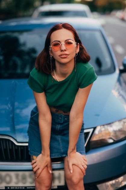 Linda garota senta-se no capô de um carro azul