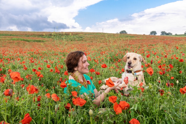 Foto linda garota senta-se no meio de um campo de papoulas e olha para o cachorro
