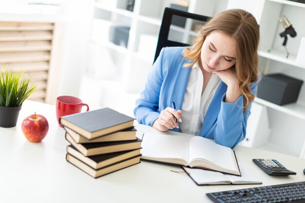 Linda garota sentada na mesa no escritório, segurando uma caneta na mão e lendo um livro.