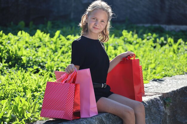 Linda garota sentada no parque com sacolas coloridas