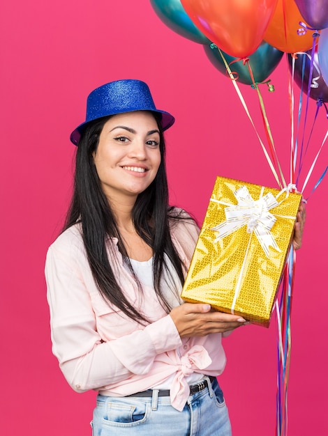 Linda garota sorridente com chapéu de festa segurando balões com uma caixa de presente