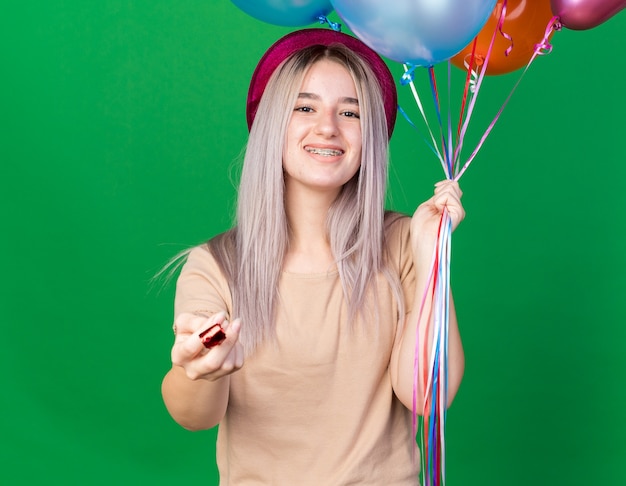 Linda garota sorridente com chapéu de festa segurando um apito de festa isolado na parede verde