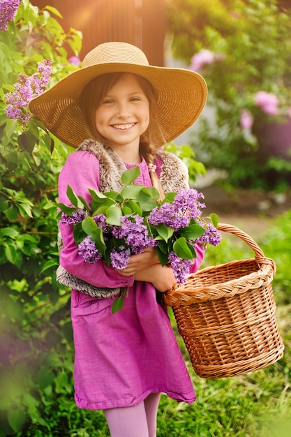 Linda garota sorridente com chapéu de palha no jardim lilás Garota com flores lilás na primavera Jardinagem