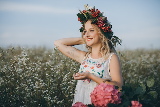 Linda garota sorridente com uma cesta de flores em um campo de camomila ao pôr do sol