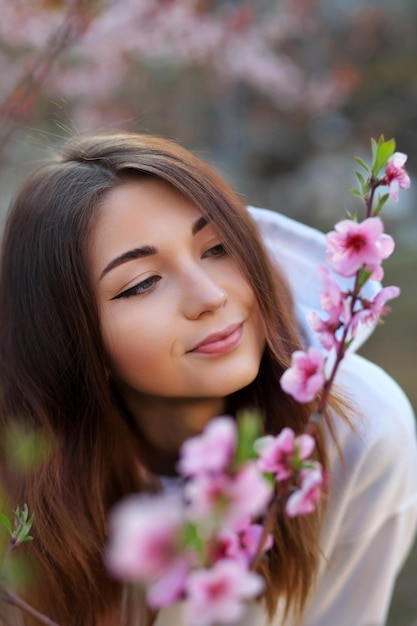 Linda garota sorridente em pé perto de um pessegueiro durante o pôr do sol Rosto feliz Tempo de primavera