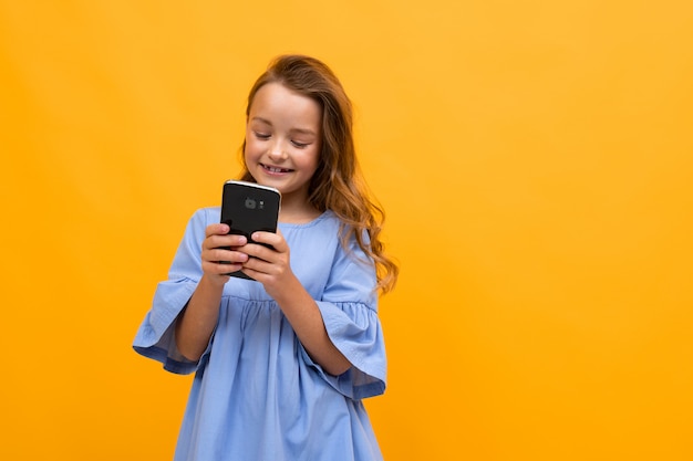 Linda garota sorridente em um vestido azul com um telefone nas mãos dela está digitando uma mensagem em um fundo amarelo