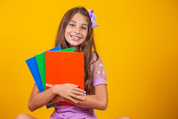 Linda garota sorridente segurando livros para a escola. fechar retrato, fundo amarelo isolado, infância. criança abraçando cadernos. estilo de vida, interesse, hobby, tempo livre, tempo livre