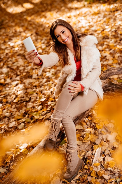 Linda garota sorridente tomando selfie na natureza no outono.