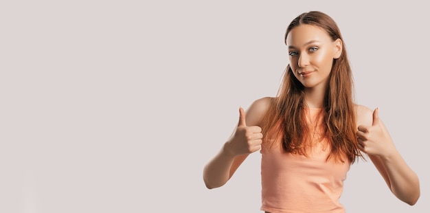 Linda garota sorrindo e mostra os polegares para cima gesto com as duas mãos em um fundo branco e isolado. mulher positiva aponta para uma ideia, um lugar para publicidade